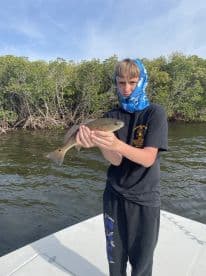 A young angler proudly displaying a Redfish while fishing in a mangrove area, showcasing the excitement of a successful catch.