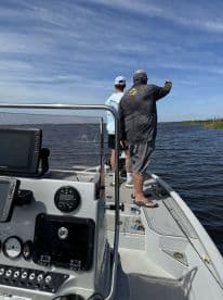 Two anglers on a boat, one pointing towards the water while the other observes, enjoying a day of fishing in a scenic waterway.