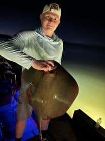 A young angler proudly displaying a large stingray caught during a night fishing trip.