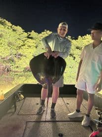 Two anglers on a boat at night, showcasing a large stingray caught during a fishing trip in a mangrove area.