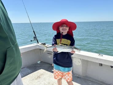 A young angler proudly displaying a caught fish while fishing on a boat in open waters.