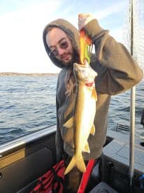 Young angler proudly holding a large Walleye while fishing on a boat, showcasing a successful catch in a scenic waterway.