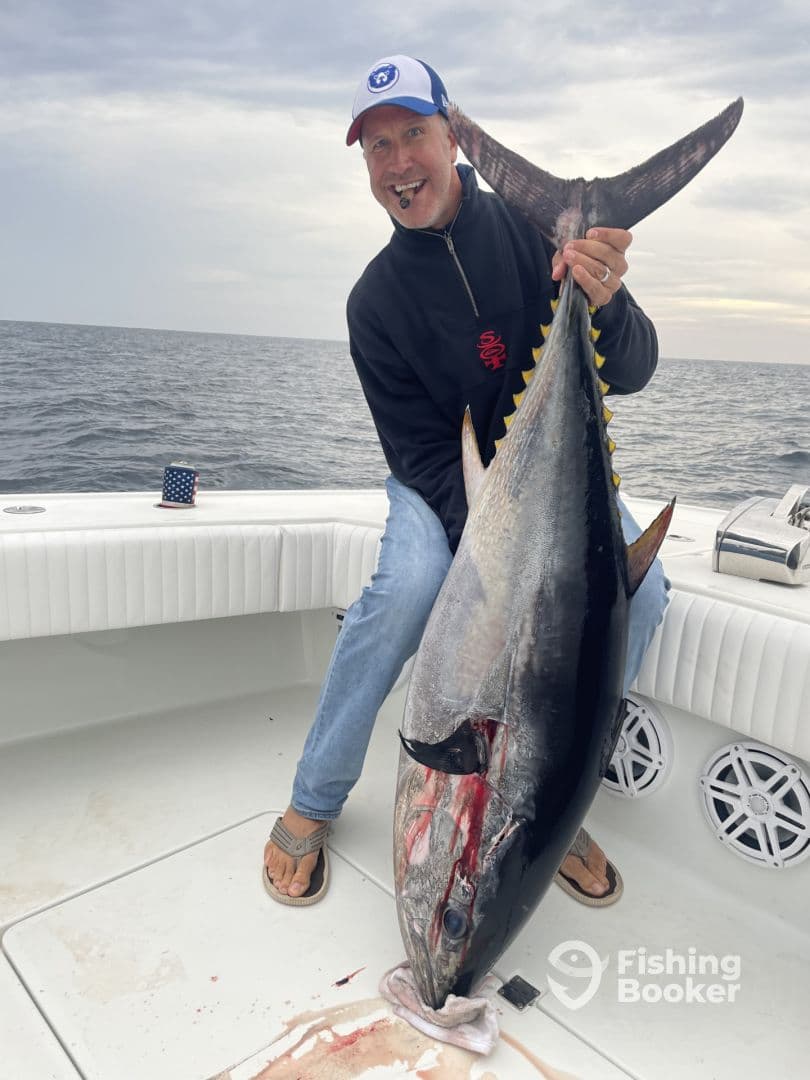 An angler proudly displaying a large Bluefin Tuna on a fishing boat, showcasing a successful offshore fishing trip.