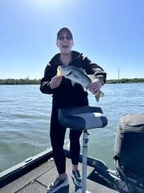 An excited angler proudly displaying a large Largemouth Bass while fishing on a sunny day.