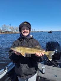 Young angler proudly holding a Walleye while fishing on a sunny day, showcasing a successful catch on the water.
