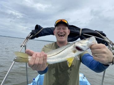 An enthusiastic angler proudly displaying a Snook while fishing from a boat in a coastal waterway.