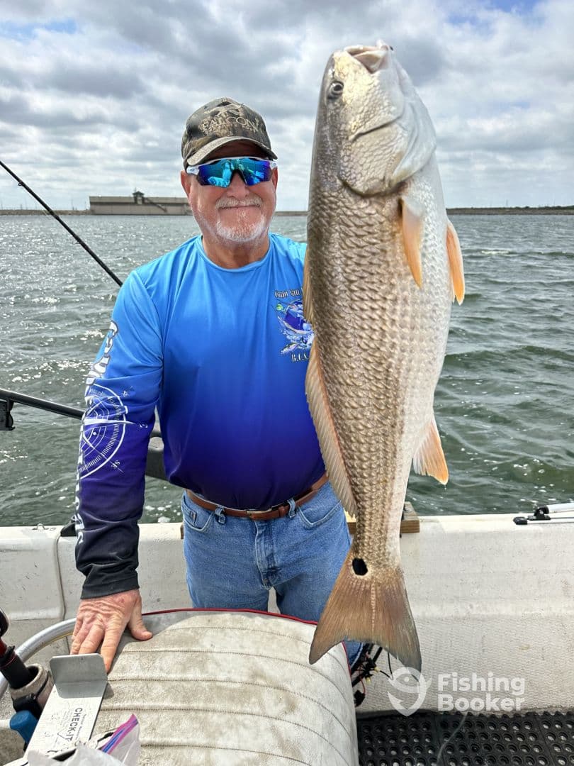 An angler proudly displaying a large Redfish while fishing on a boat, showcasing a successful day on the water.