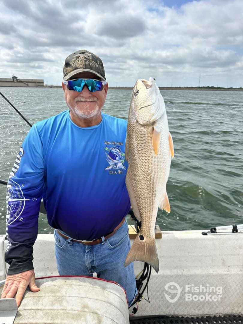 An angler proudly displaying a large Redfish while fishing on a boat, showcasing a successful day on the water.