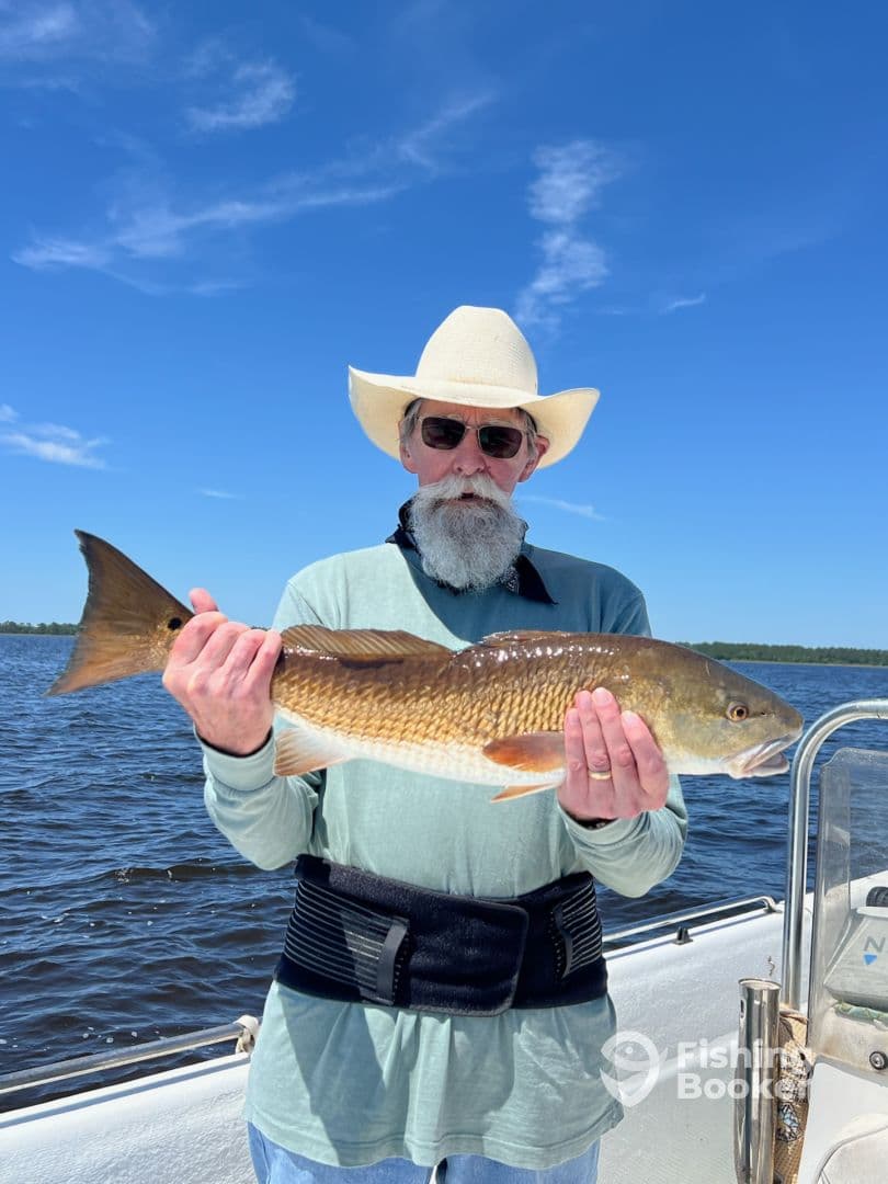 An angler proudly displaying a large Redfish while enjoying a sunny day on the water.