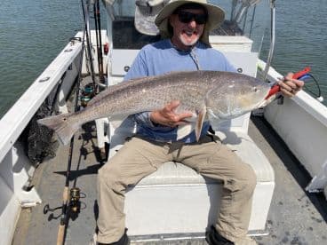 An angler proudly displaying a large Redfish while seated on a fishing boat, showcasing a successful day on the water.