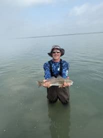 Angler standing in shallow water proudly displaying a Redfish caught during a coastal fishing trip.