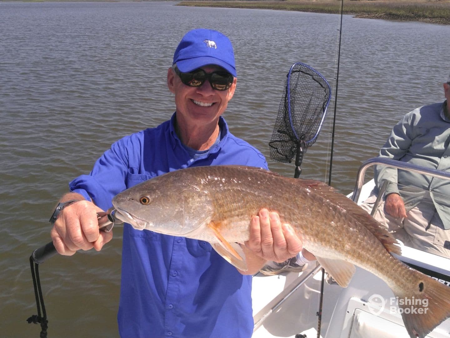 An angler proudly displaying a large Redfish while fishing on a boat in a coastal waterway.