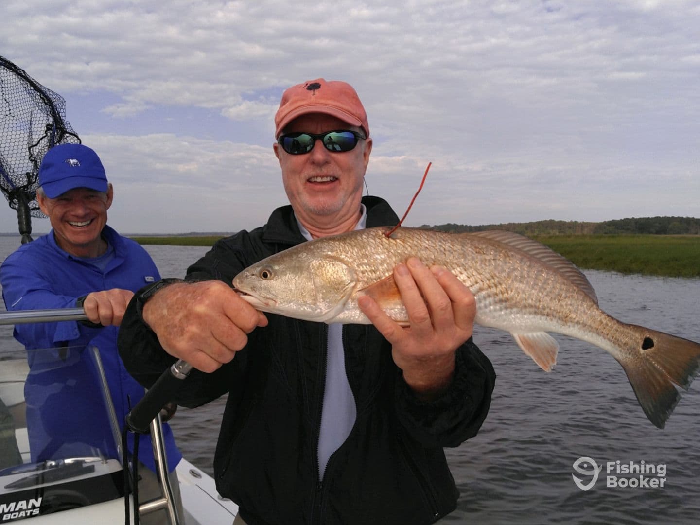 Two anglers enjoying a successful fishing trip, with one proudly displaying a large Redfish against a scenic backdrop.