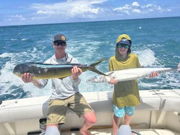 A proud moment on the water as an adult and a young angler display their catches, a Mahi Mahi and a Barracuda, during a fishing trip.