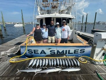 A group of anglers proudly posing with their catch of Spanish Mackerel on the dock next to the 'Sea Smiles' charter boat in North Carolina.