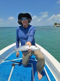An angler proudly displaying a caught fish on a sunny day while fishing from a small boat in clear waters.