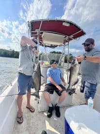 Two anglers proudly displaying their catches of catfish while seated on a boat during a fishing trip.