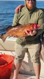 Angler proudly displaying a large Red Grouper while fishing offshore, with a vibrant ocean backdrop.