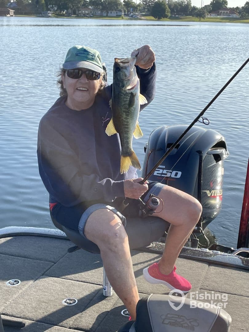 An angler proudly displaying a large Largemouth Bass while fishing from a boat on a calm lake.