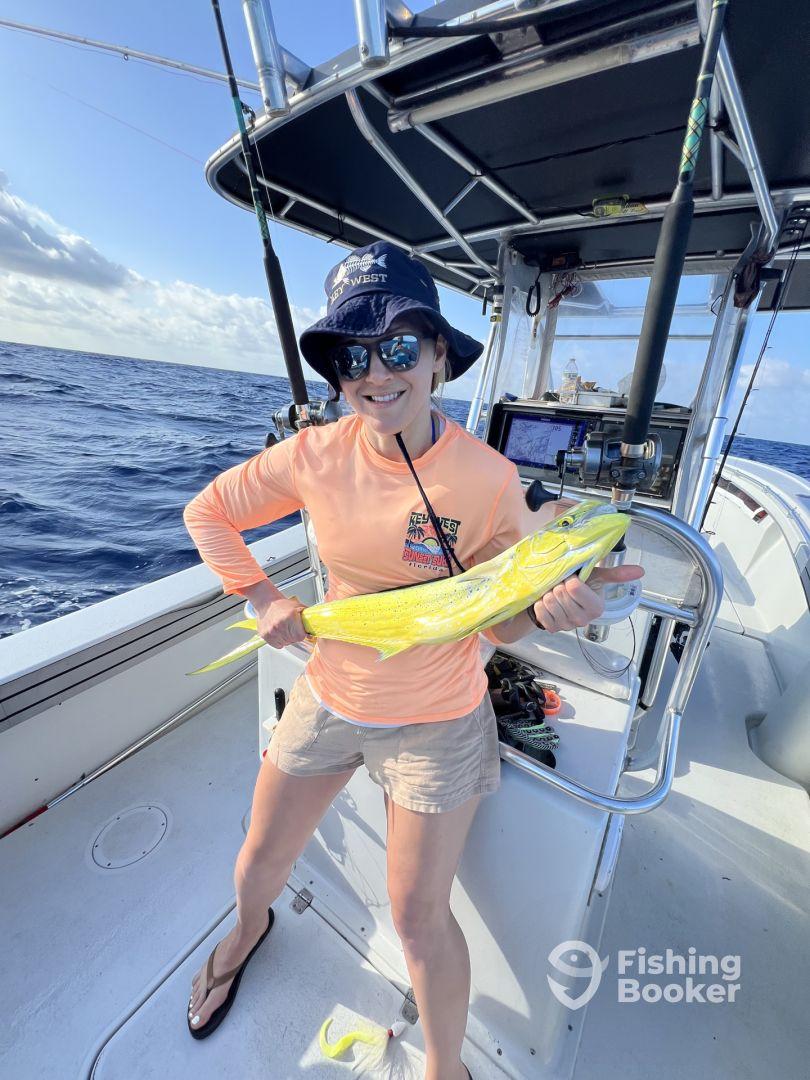 An angler proudly displaying a vibrant Mahi Mahi aboard a fishing boat in open waters, showcasing a successful day of deep-sea fishing.