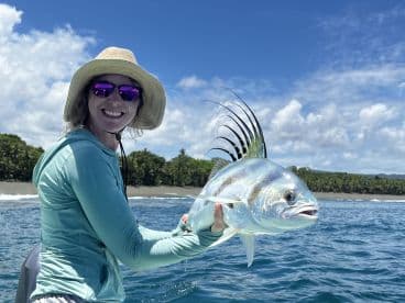 A smiling angler proudly displaying a beautiful Roosterfish while fishing in a tropical setting.