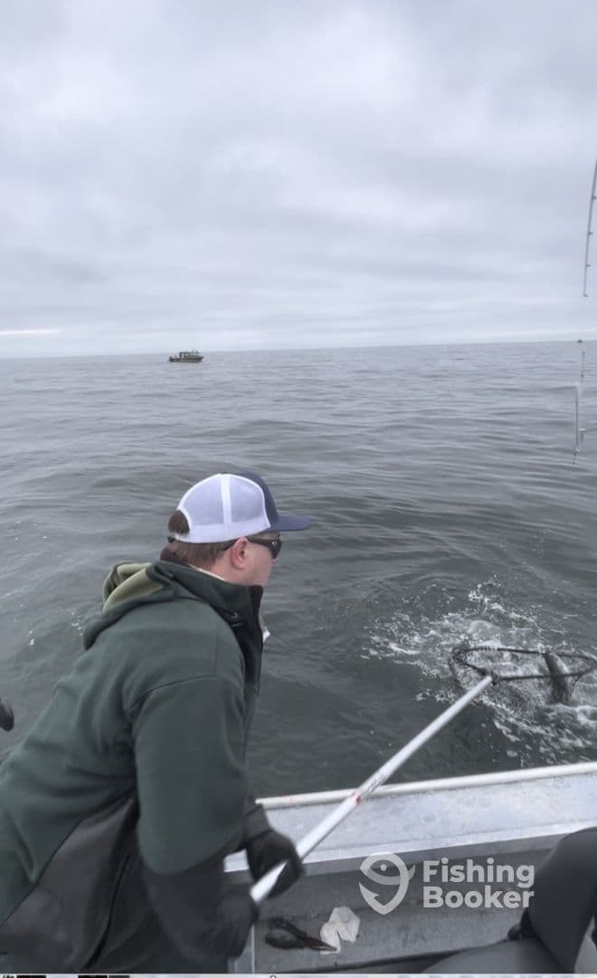 A young angler is actively reeling in a fish while fishing on a boat in overcast conditions, showcasing the excitement of the catch.