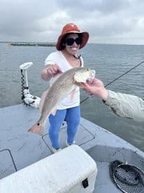 An excited angler proudly displaying a Redfish while fishing on a boat in a coastal waterway.