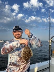 Angler proudly displaying a Flounder while fishing on a boat under a clear sky.