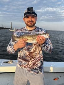 Angler proudly displaying a Speckled Trout while fishing from a boat in a coastal waterway.