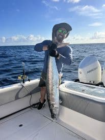 Angler proudly displaying a large Kingfish aboard a boat in open waters, showcasing a successful offshore fishing trip.