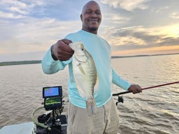 An angler proudly displaying a freshly caught Crappie while fishing on a serene lake at sunset.