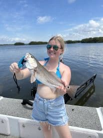 A young woman proudly displaying a Redfish while fishing in a scenic coastal environment.