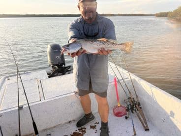 Angler proudly displaying a Speckled Trout while fishing from a small boat in calm waters.