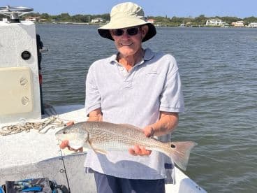 An older angler proudly displaying a Redfish while fishing from a boat in a coastal waterway.