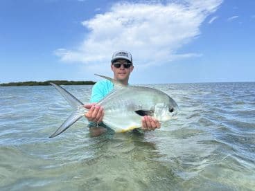 Angler holding a beautiful Permit while wading in shallow waters, showcasing a successful day of fishing in a tropical environment.