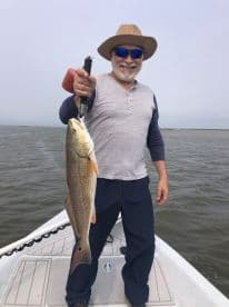 An angler proudly displaying a large Redfish while fishing from a boat in a coastal waterway.