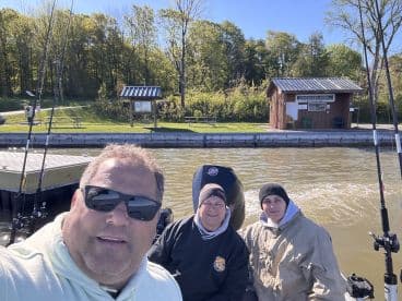 Three anglers enjoying a day on the water, seated in a boat with fishing rods ready for action, set against a scenic backdrop.