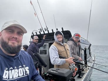 Four anglers on a fishing boat, actively engaged in fishing with rods in hand, showcasing a cloudy day on the water.