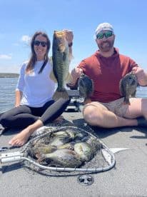 Two anglers proudly displaying their catch, including a large Largemouth Bass and several Bluegill, while fishing on a sunny day.