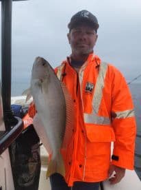 An angler proudly displaying a large fish while fishing on a boat in overcast conditions.