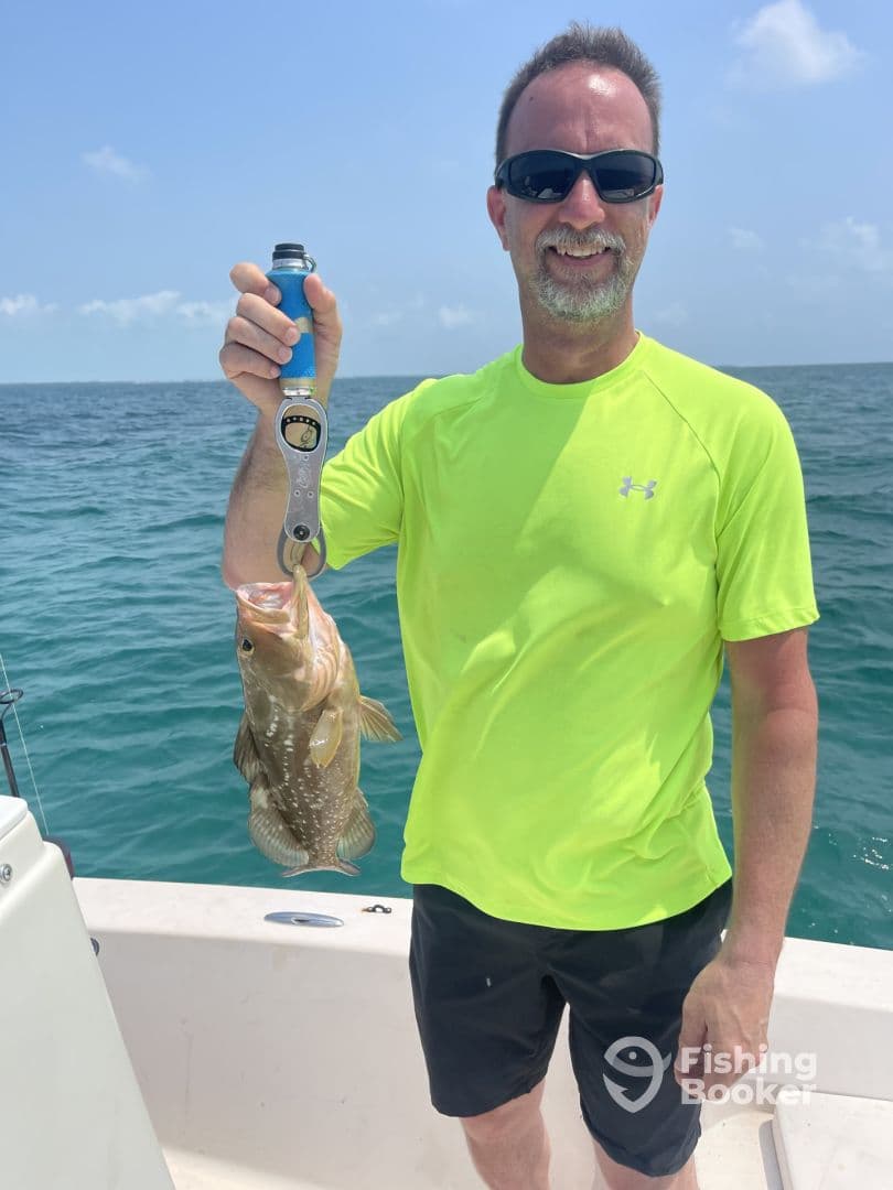 An angler proudly displaying a large Grouper while fishing on a sunny day in open waters.