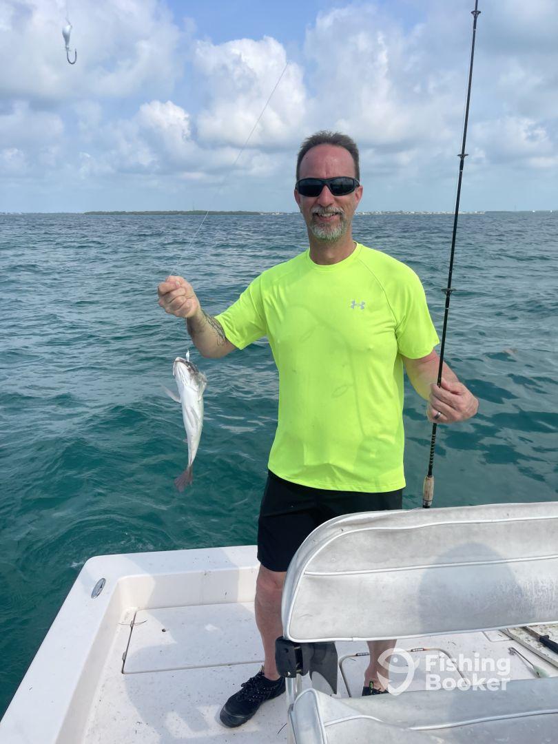 An angler proudly displaying a freshly caught fish while fishing from a boat in clear blue waters.