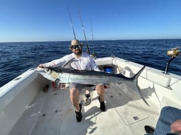 An angler proudly displaying a large Marlin aboard a fishing boat in open waters, showcasing a successful deep-sea fishing trip.