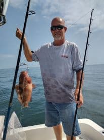 An angler proudly displaying a large Grouper caught while fishing offshore, showcasing a sunny day on the water.