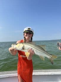 A smiling angler proudly displays a large Snook while wearing a captain's hat on a fishing trip.