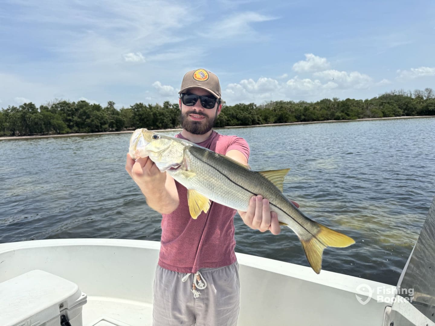 An angler proudly displaying a large Snook while fishing from a boat in a scenic coastal environment.