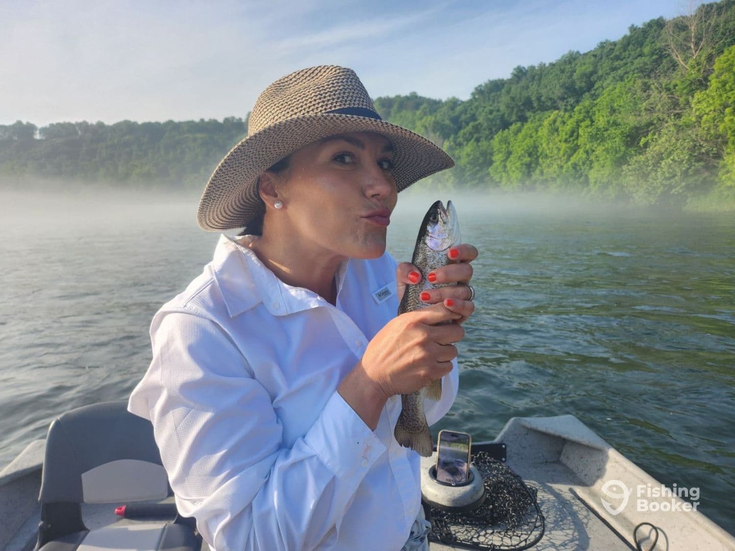 An angler enjoying a serene morning on the water, proudly holding a freshly caught trout while surrounded by lush greenery.