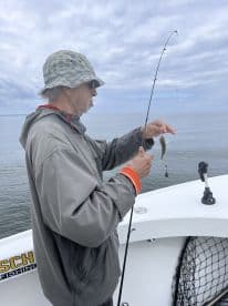 An angler reeling in a small fish while fishing from a boat, showcasing the excitement of the catch in calm waters.