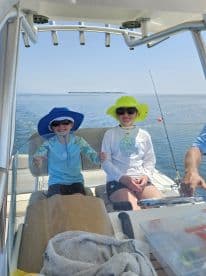 Two young anglers enjoying a day on the water, seated in the helm of a fishing boat, ready for an adventure.