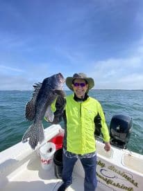 Angler proudly displaying a large Black Sea Bass while fishing on a sunny day.